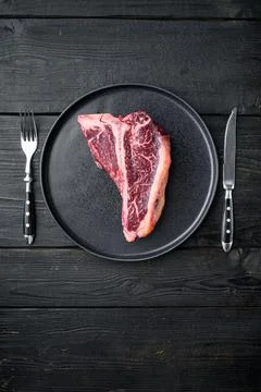 Raw fresh dry aged beef T-bone steak, on plate, on black wooden table backgro Stock Photos