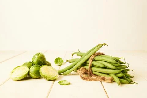 Raw Green beans tied with at string and Brussel sprouts placed on wooden table Stock Photos