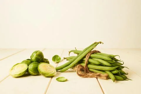Raw Green beans tied with at string and Brussel sprouts placed on wooden table Stock Photos