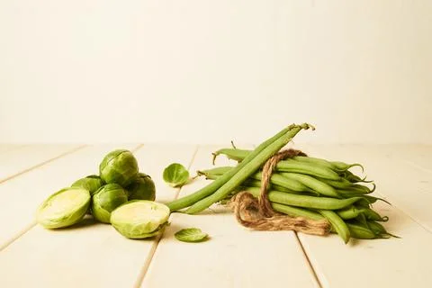 Raw Green beans tied with at string and Brussel sprouts placed on wooden table Stock Photos