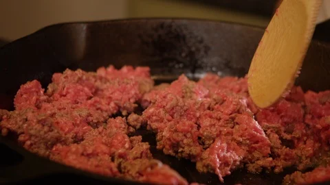Raw ground beef cooking in cast iron skillet with wooden spoon Stock Footage 114509087