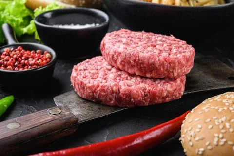Raw ground beef cutlets with ingredients for burger on black background Stock Photos