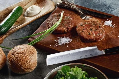 Raw Ground beef meat Burger steak cutlets with ingredients on the board. Stock Photos