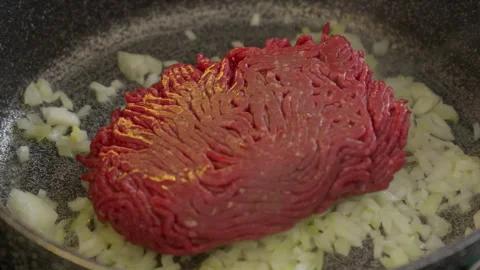 Raw ground beef meat dropped on top of diced onion in in gray frying pan skillet Stock Footage 266782657