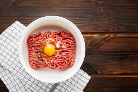 Raw ground beef or minced beef in a white bowl on wooden background. Top view Foto stock