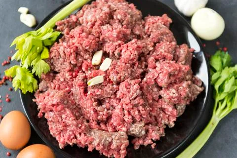 Raw ground beef in a plate, celery, garlic cloves, eggs onion, meat Stock Photos