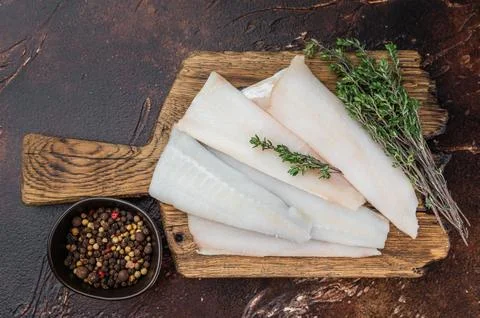 Raw hake, cod or pollock fillets with thyme on wooden board over dark kitch.. 스톡 사진
