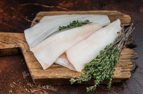 Raw hake, cod or pollock fillets with thyme on wooden board over dark kitch.. Stock Photos
