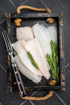 Raw hake or pollock fillets with rosemary on rustic wooden tray. Fresh cod .. Stock Photos