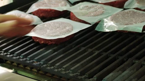 Raw hamburger patties being placed on a hot char broiler Stock Footage 127715952
