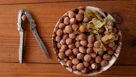 Raw hazelnuts in porcelain bowl with nutcracker on rustic wooden background Stock Footage 139267307