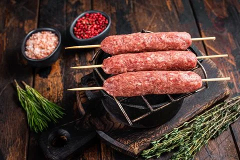 Raw kofta or lula kebabs skewers on a grill with herbs. Dark wooden background Stock Photos
