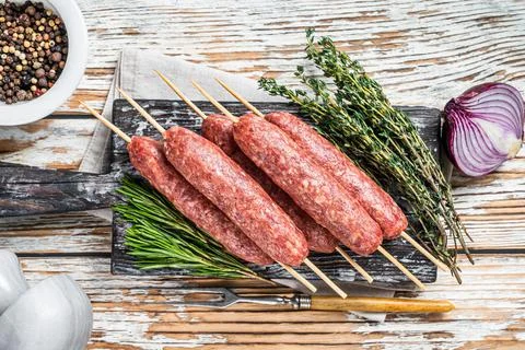 Raw kofta or lula kebabs meat sausages on skewers with herbs. Dark wooden Stock Photos