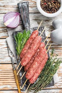 Raw kofta or lula kebabs meat sausages on skewers with herbs. Dark wooden Stock Photos