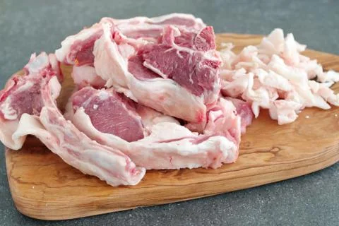 Raw lamb chops and fat on a olive wood cutting board on a grey background Stock Photos