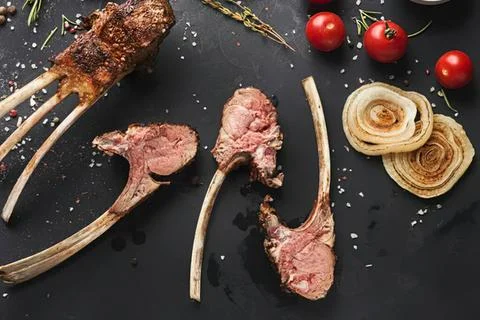 Raw lamb chops with onion and cherry tomatoes on black Stock Photos