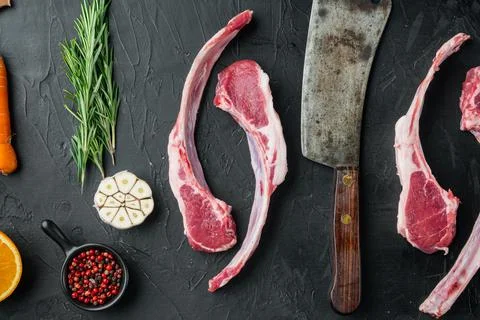 Raw lamb chops or mutton cuts, with ingredients carrot orange, herbs, on blac Stock Photos