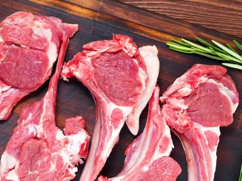 Raw lamb cutlets on bone on dark brown wooden background, lamb ribs, top view. Stock Photos
