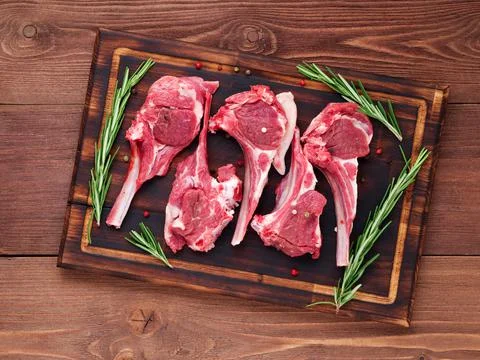 Raw lamb cutlets on bone on dark brown wooden background, lamb ribs, top view. Stock Photos