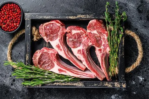 Raw lamb meat chops steaks in a wooden tray. Black background. Top view Stock Photos