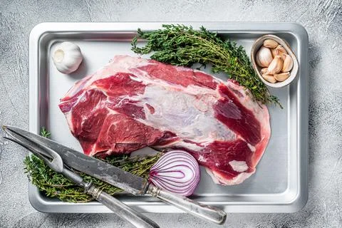 Raw lamb mutton shoulder meat in a baking dish with thyme and garlic. White Stock Photos