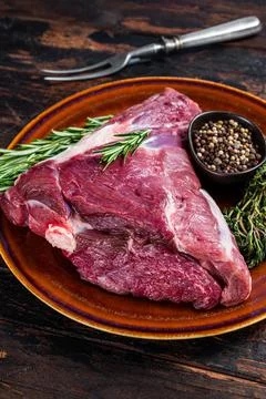 Raw lamb mutton thigh or leg with rosemary and thyme in rustic plate. Dark Stock Photos