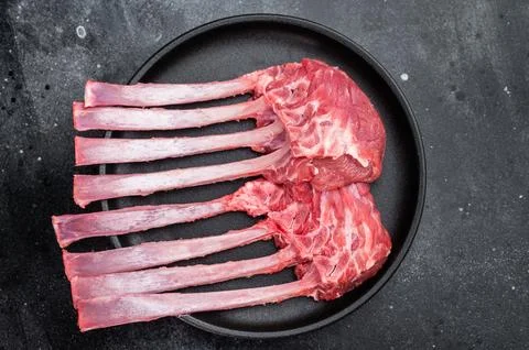 Raw lamb rack ribs with bone on cast iron skillet dark stone background top.. Stock Photos