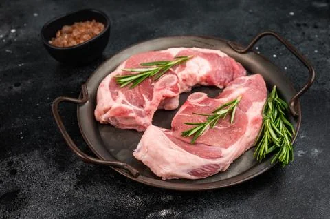 Raw lamb rump steak with bone served in rustic metal pan with fresh rosemar.. Stock Photos