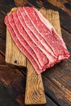 Raw marbled beef bacon slices on rustic wooden board with herbs and pepper,.. Stock Photos