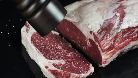 Raw marbled ribeye beef steak sprinkled with seasoning on black table top Stock Footage 169721826