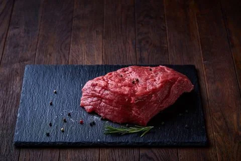 Raw meat beef steaks on black slate board with spices and rosemary over wooden Stock Photos