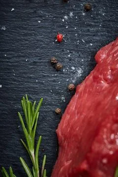 Raw meat beef steaks on black slate board with spices and rosemary over wooden Stock Photos