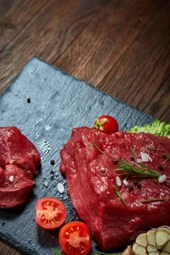 Raw meat beef steaks on black slate board with spices, garlic and rosemary over Stock Photos