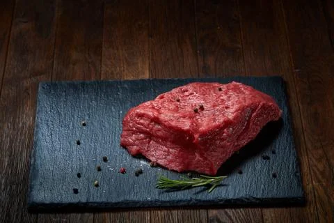 Raw meat beef steaks on black slate board with spices and rosemary over wooden Stock Photos