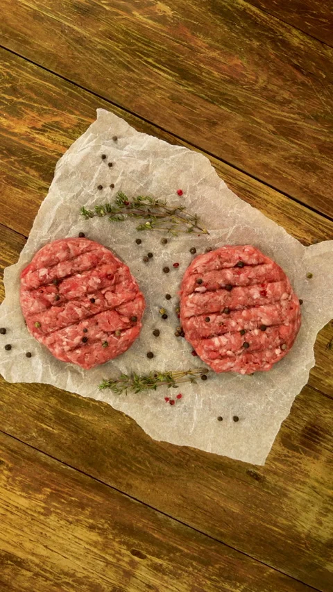 Raw meat burger cutlets, with spices and thyme sprigs rotate on crumpled paper. Stock Footage 232030739