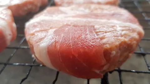 Raw meat cutlets wrapped in bacon are cooked on the grill rack. The chef pr.. Stock Photos