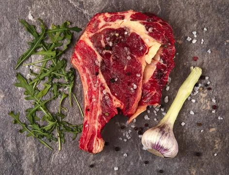 Raw meat on a gray background. Garlic, arugula. Top. Stock Photos