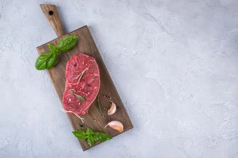 Raw meat. Raw beef steak on a cutting board with greens and spices. Stock Photos