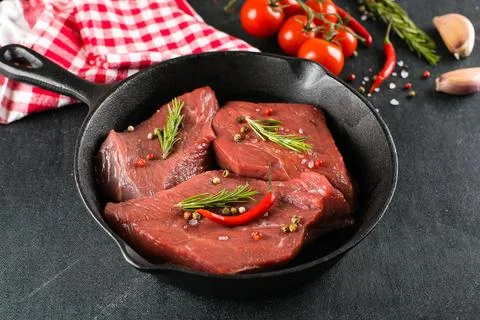 Raw meat. Raw beef steak in pan with herbs and spices on a black background.. Stock Photos