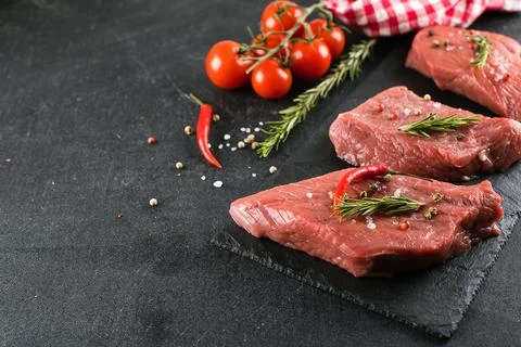 Raw meat. Raw beef steak on a black board with herbs and spices. Top view. Stock Photos