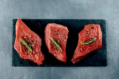 Raw meat. Raw beef steak on a black board with herbs and spices. Top view. Stock Photos