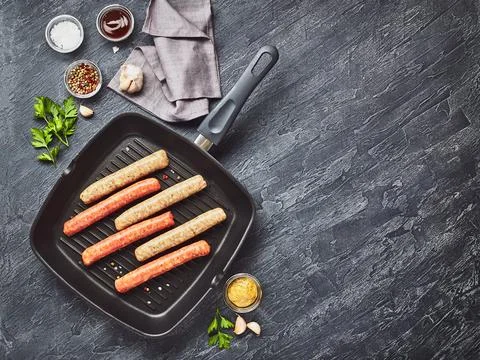Raw meat sausages on square grill pan, with herbs and spices. Top view Stock Photos