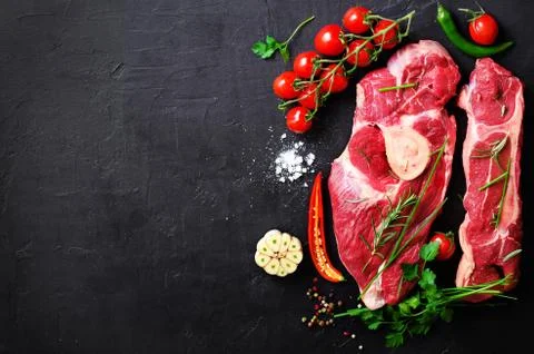 Raw meat steaks with cherry tomatoes, hot pepper, garlic, oil and herbs on dark Stock Photos