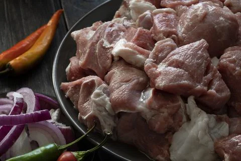 Raw mutton cut into medium pieces, laid on a plate, surrounded by red onions Фото