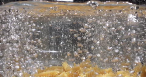 Raw pasta fall into boiling water in pot on kitchen stove. Camera follows Stock-Footage 254546153