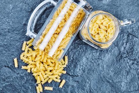 Raw pasta inside the two glass jars on blue background Stock Photos