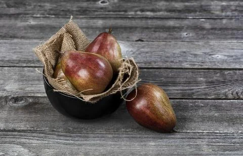Raw pears inside and outside of bowl on aged wooden table in close up view Stock Photos