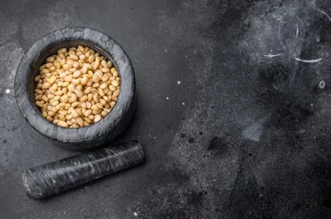 Raw pine nuts placed in a grey stone mortar on a deep textured black backdr.. Stock Photos