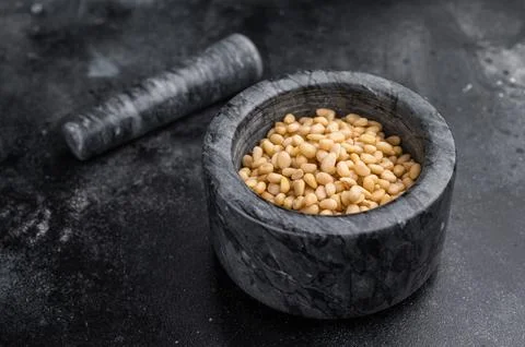 Raw pine nuts placed in a grey stone mortar on a deep textured black backdr.. Stock Photos