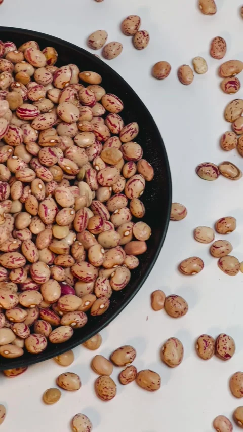 Raw pinto beans in dark plate, white background, vertical format, top view Stock Footage 336471799